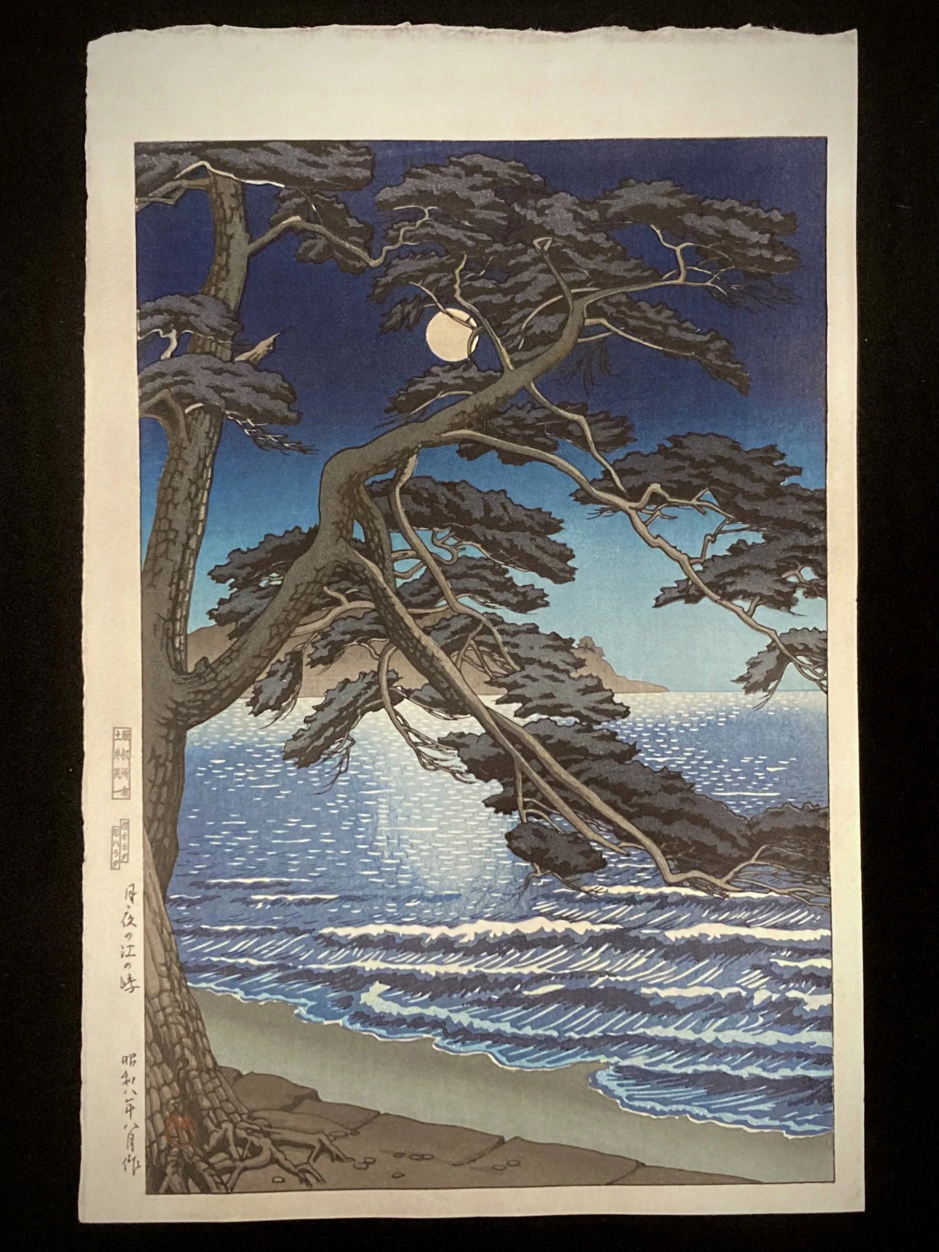 Japanese woodblock print by Kawase Hasui showing a moonlit night at Enoshima Beach, with a gnarled pine tree framing the full moon and a calm sea.
