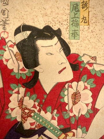 Close-up of Japanese art print featuring a Kabuki actress’s intense gaze and red kimono with white floral motifs, showcasing Ukiyo-e linework and drama.
